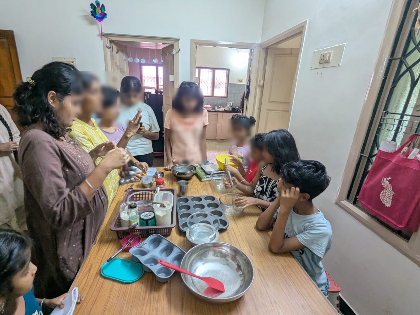 An adult measuring out batter into baking tins while children watch from around the table
