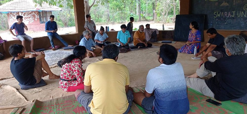 Adults sitting in a circle on the floor of an open hall, in discussion