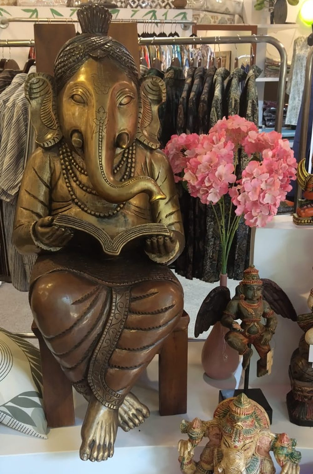 A brass and wood sculpture of Ganesha seated on a stool, absorbed in an open book held in both hands